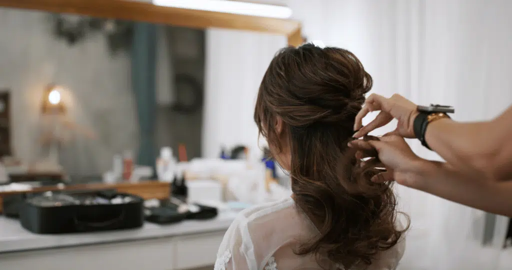 Hairdresser making hairstyle on bride in beauty salon