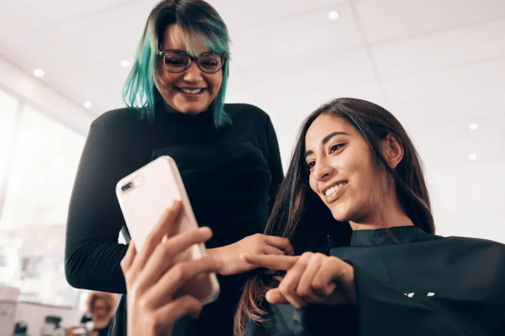 salon client using social media on the phone while stylist smiles