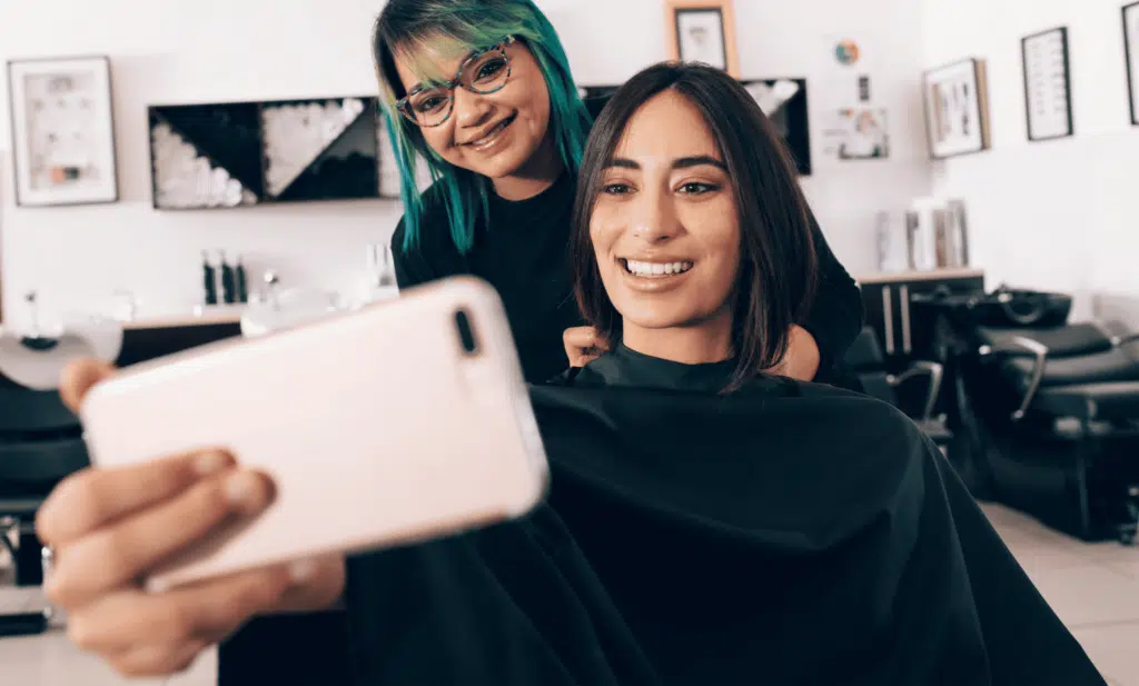 client taking selfie at a hair salon with stylist behind