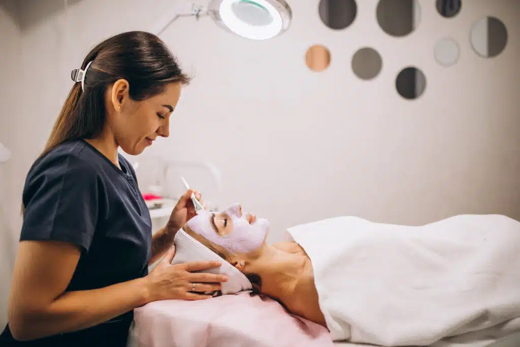 cosmetologist applying mask on a face of client in a beauty salon