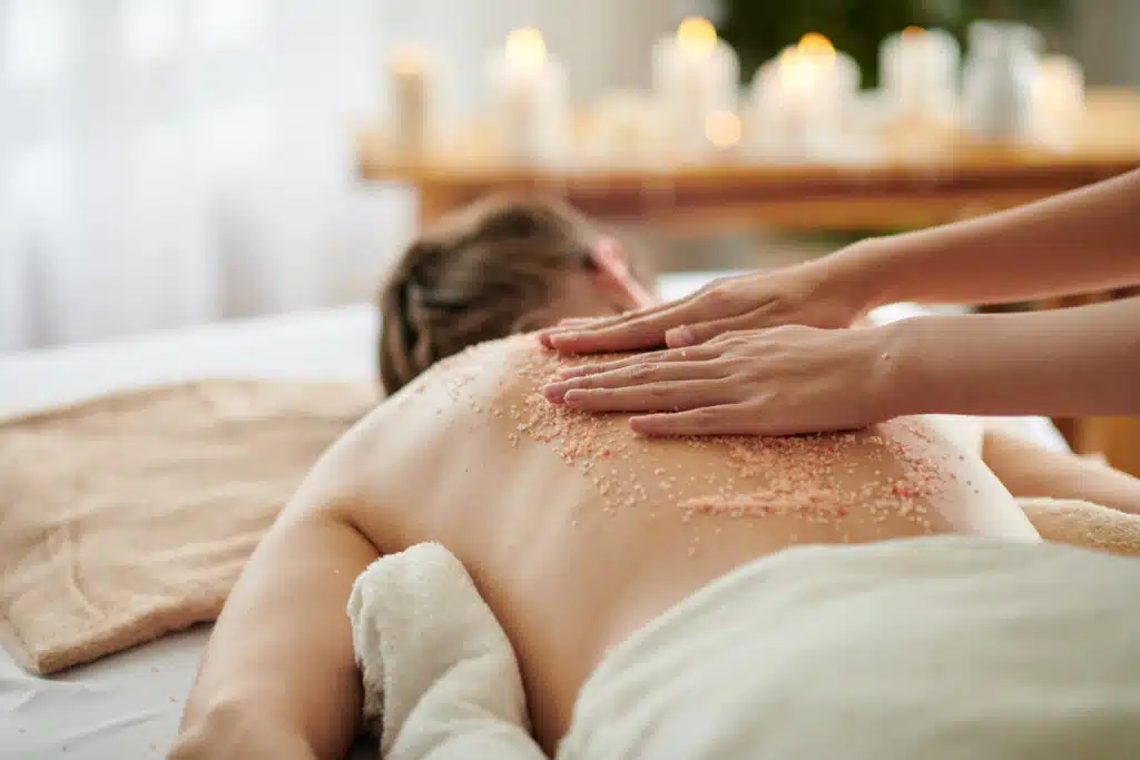 Close-up image of esthetician scrubbing back of female client to get rid of dead skin cells