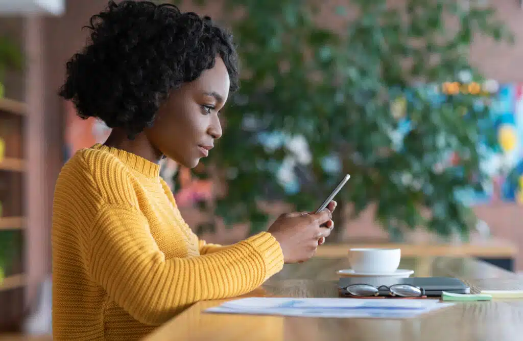 afro american girl receiving message on the phone with some belongings on the table